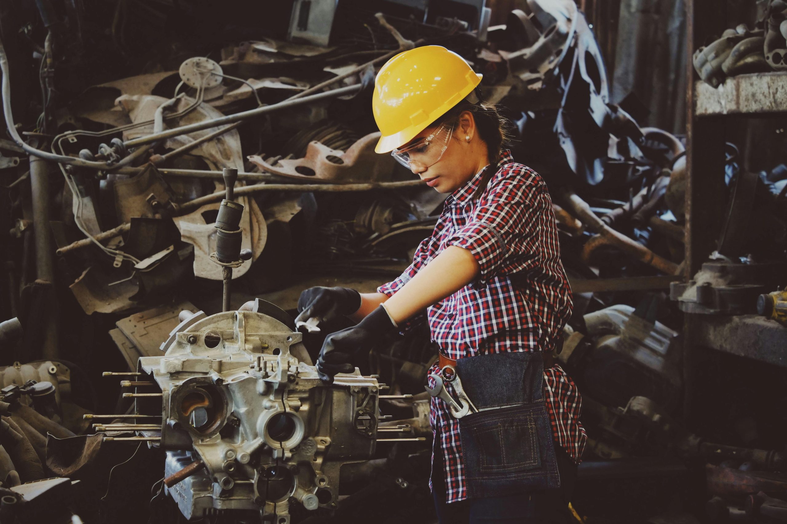 Woman engineer wearing safety gear, working on machine repair in an industrial setting.